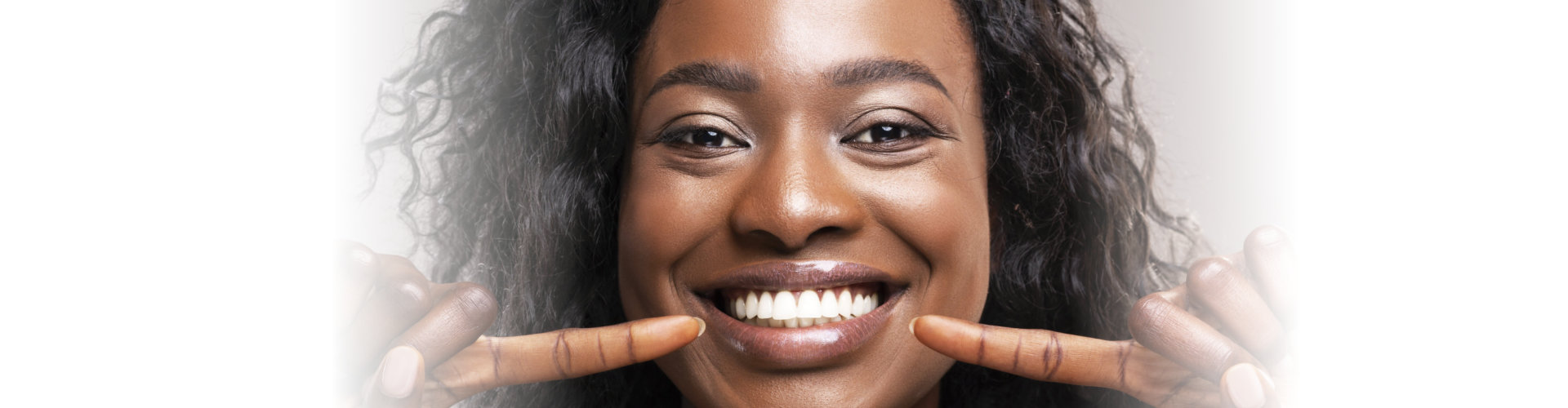 Teeth alignment and whitening concept. Happy african american girl pointing at her wide smile with two forefingers over grey background, closeup