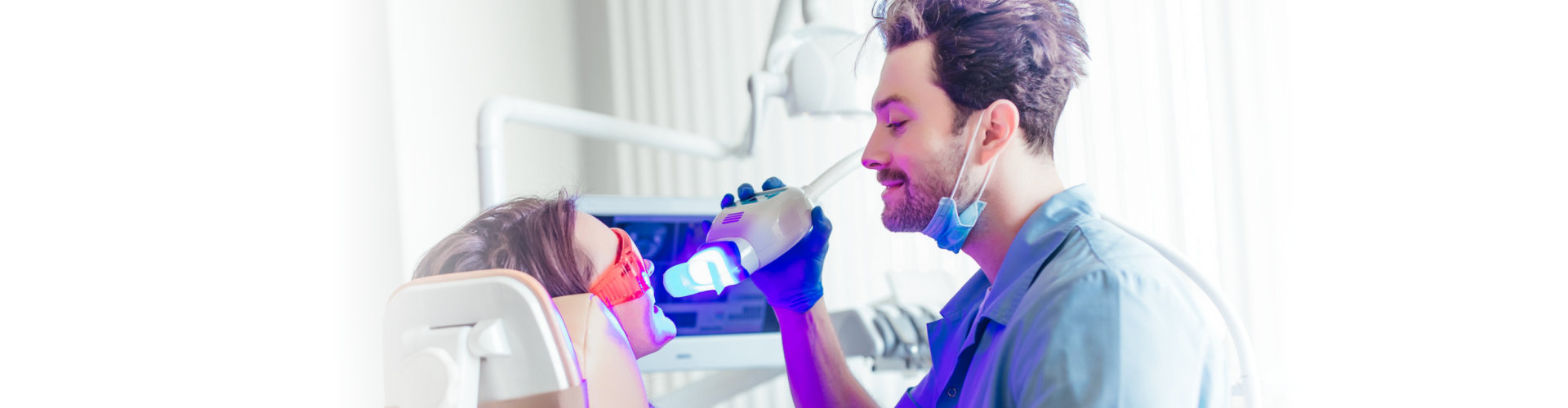 Portrait of a female patient at dentist in the clinic. Teeth whitening procedure with ultraviolet light UV lamp.