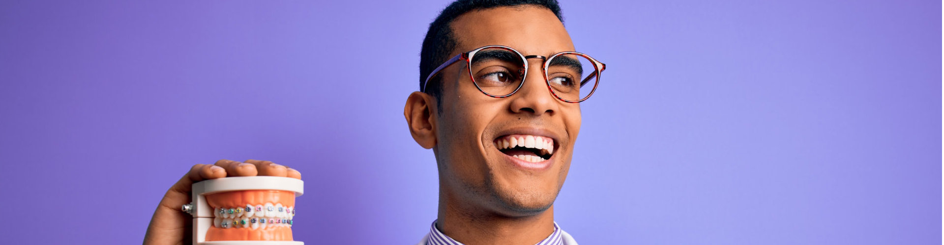 Young handsome african american dentist man holding denture teeth with dental braces pointing and showing with thumb up to the side with happy face smiling